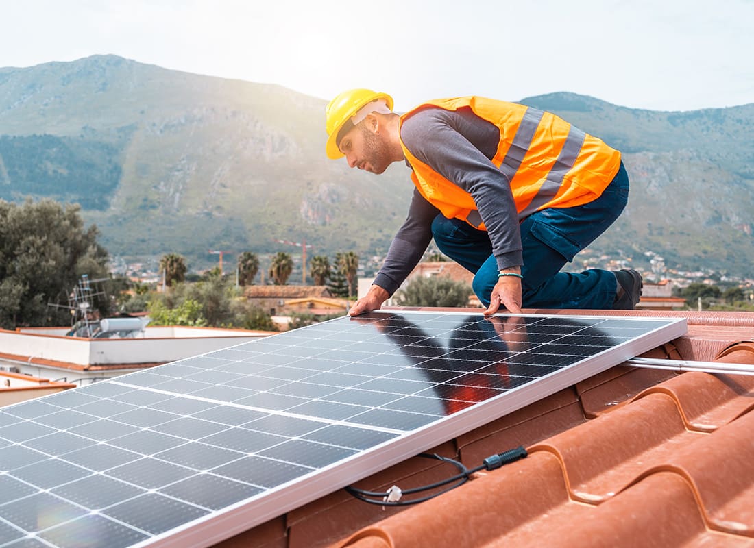 Insurance by Industry - Contractor Installing a Solar Panel on Top of a Roof With Mountains in the Background